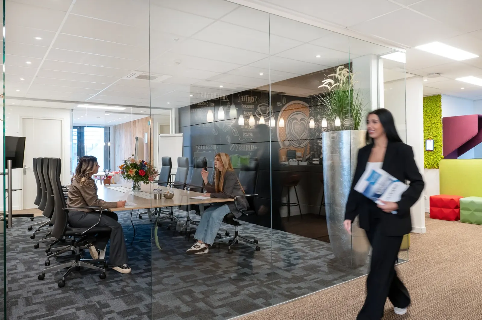Vergaderzaal met glazen wand waarin vier mensen rond een lange tafel overleggen in Office Capital Hasselt