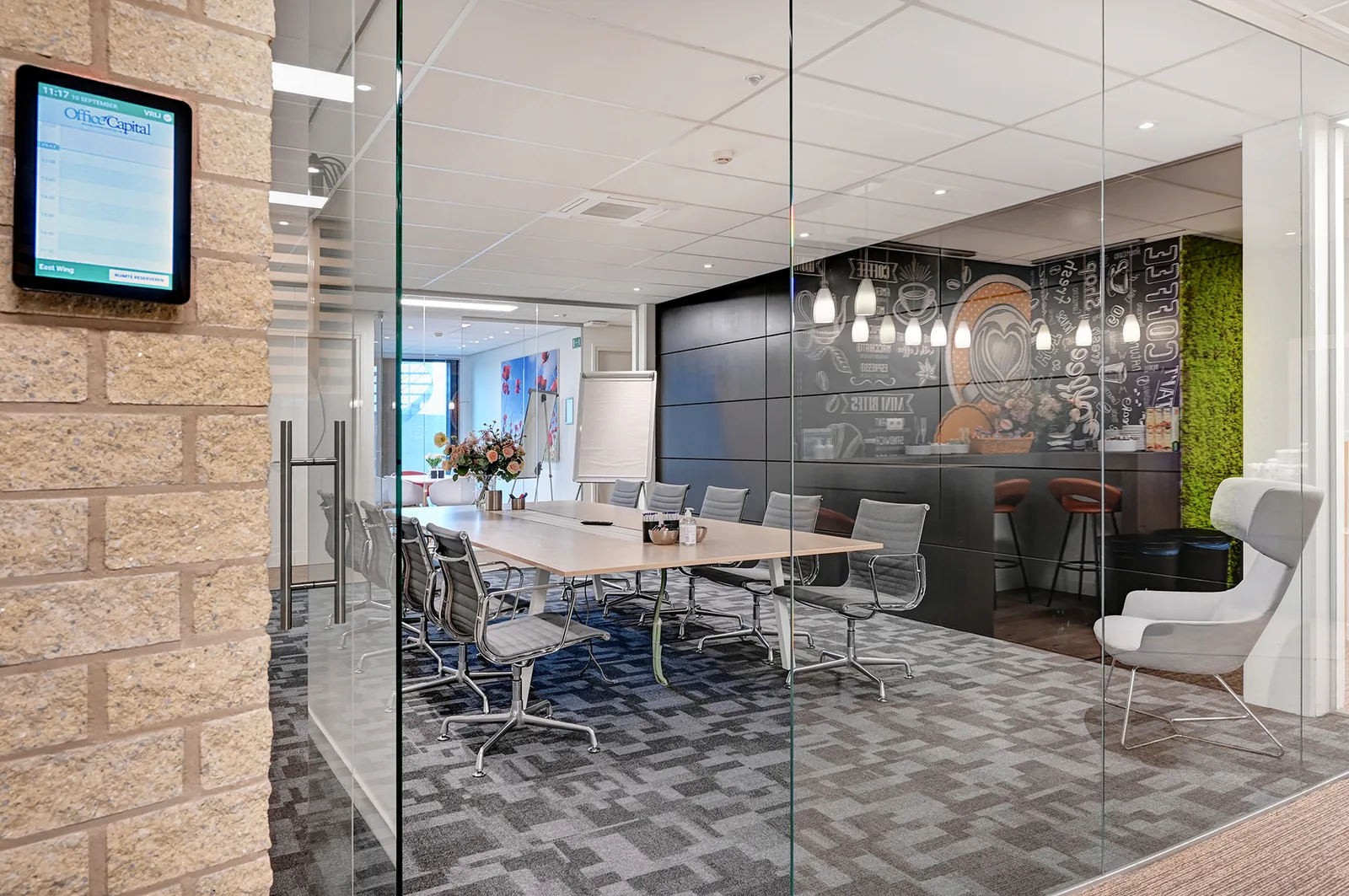 Vergaderruimte met glazen wand en houten tafel, met doorkijk naar de koffiecorner in Office Capital Hasselt