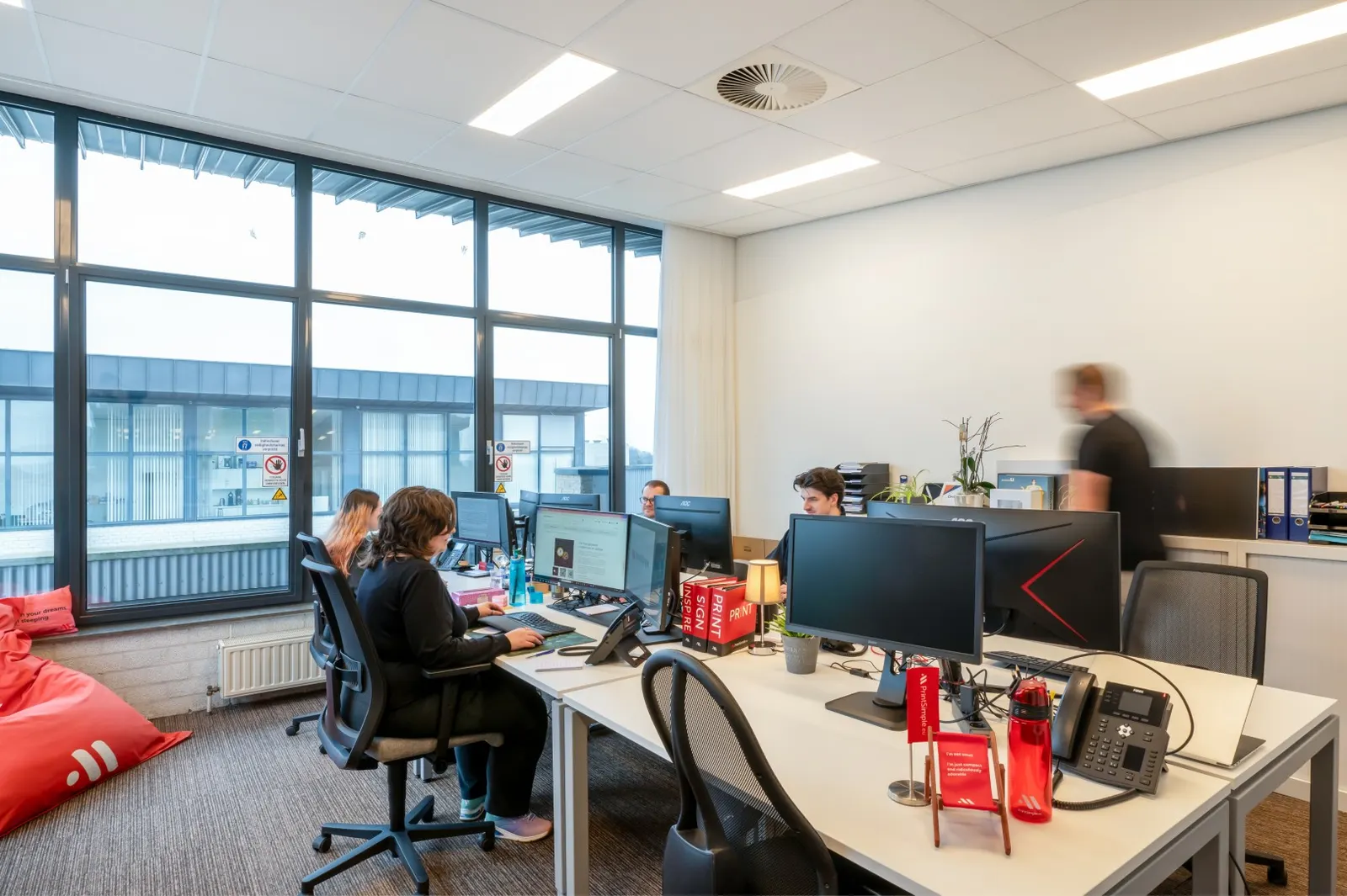 Werkruimte met bureaus, beeldschermen en een rode zitzak in Office Capital Hasselt