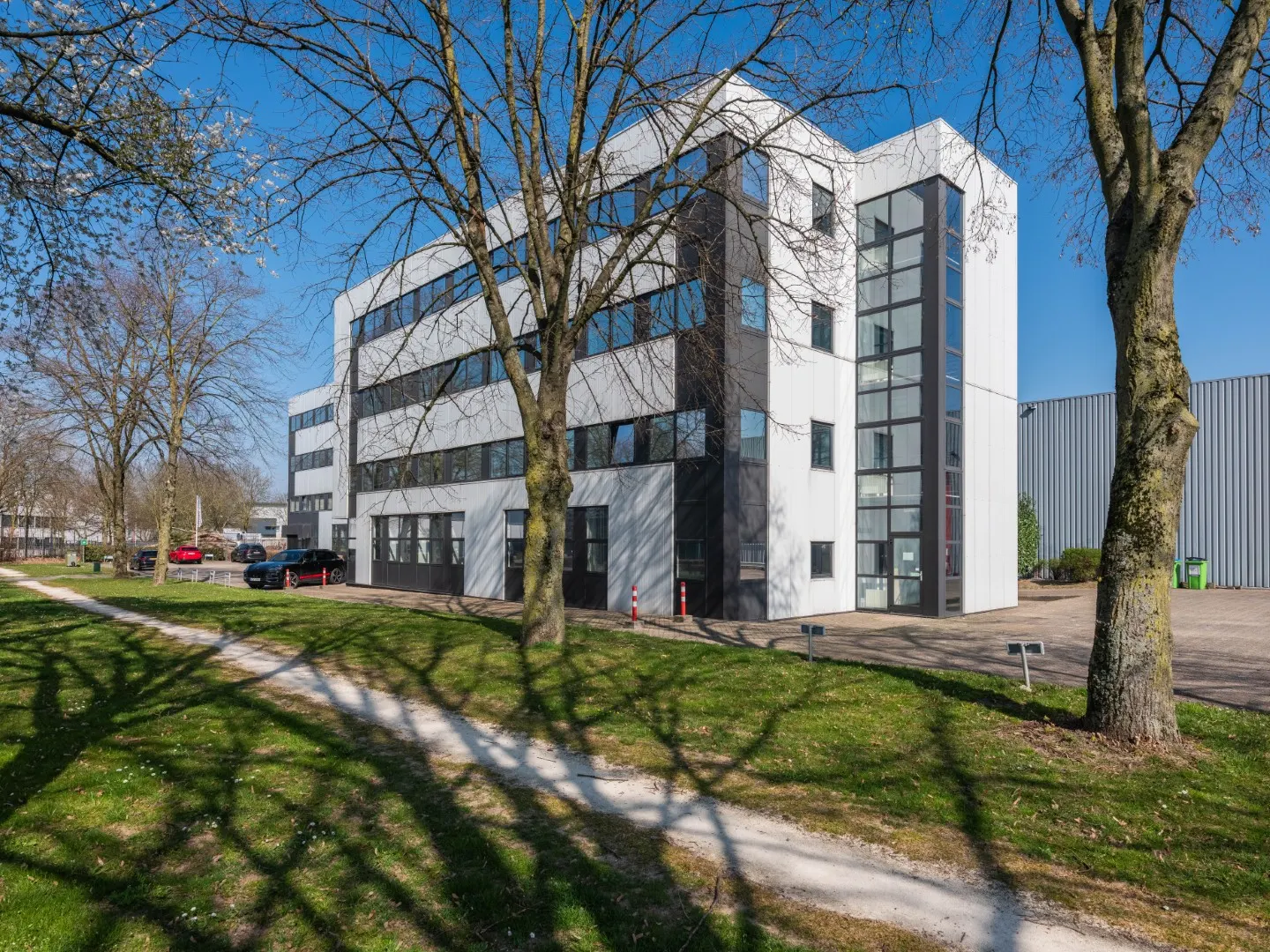 Het kantoorgebouw van Office Capital Maastricht-Airport gezien vanaf het grasveld met bomen