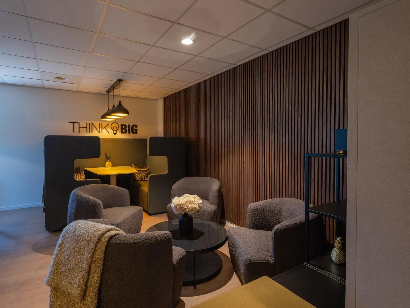 Loungeruimte met fauteuils, salontafel en de muurtekst Think Big in Office Capital Maastricht-Airport