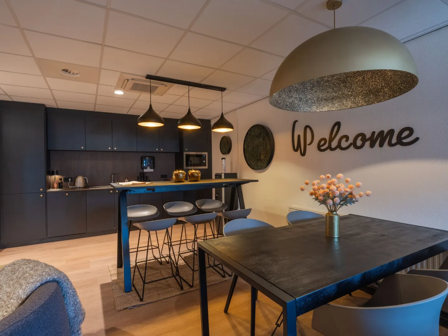 Koffiecorner met hoge bar, eettafel en de muurtekst Welcome in Office Capital Maastricht-Airport