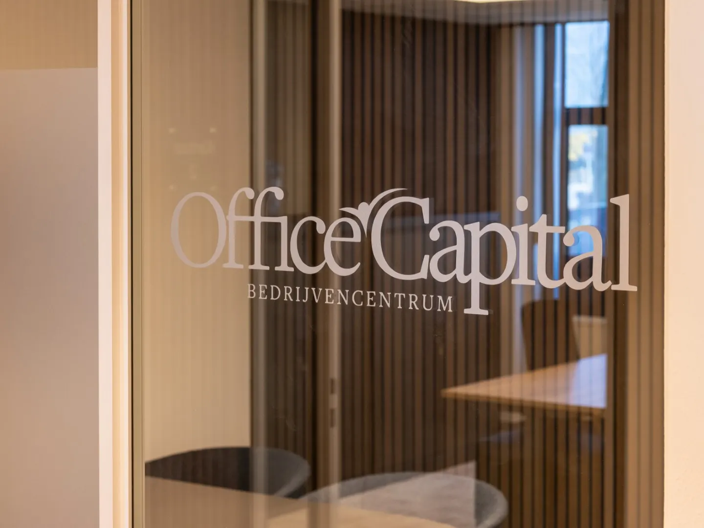 Glazen wand met het logo van Office Capital in de gang van Maastricht-Airport