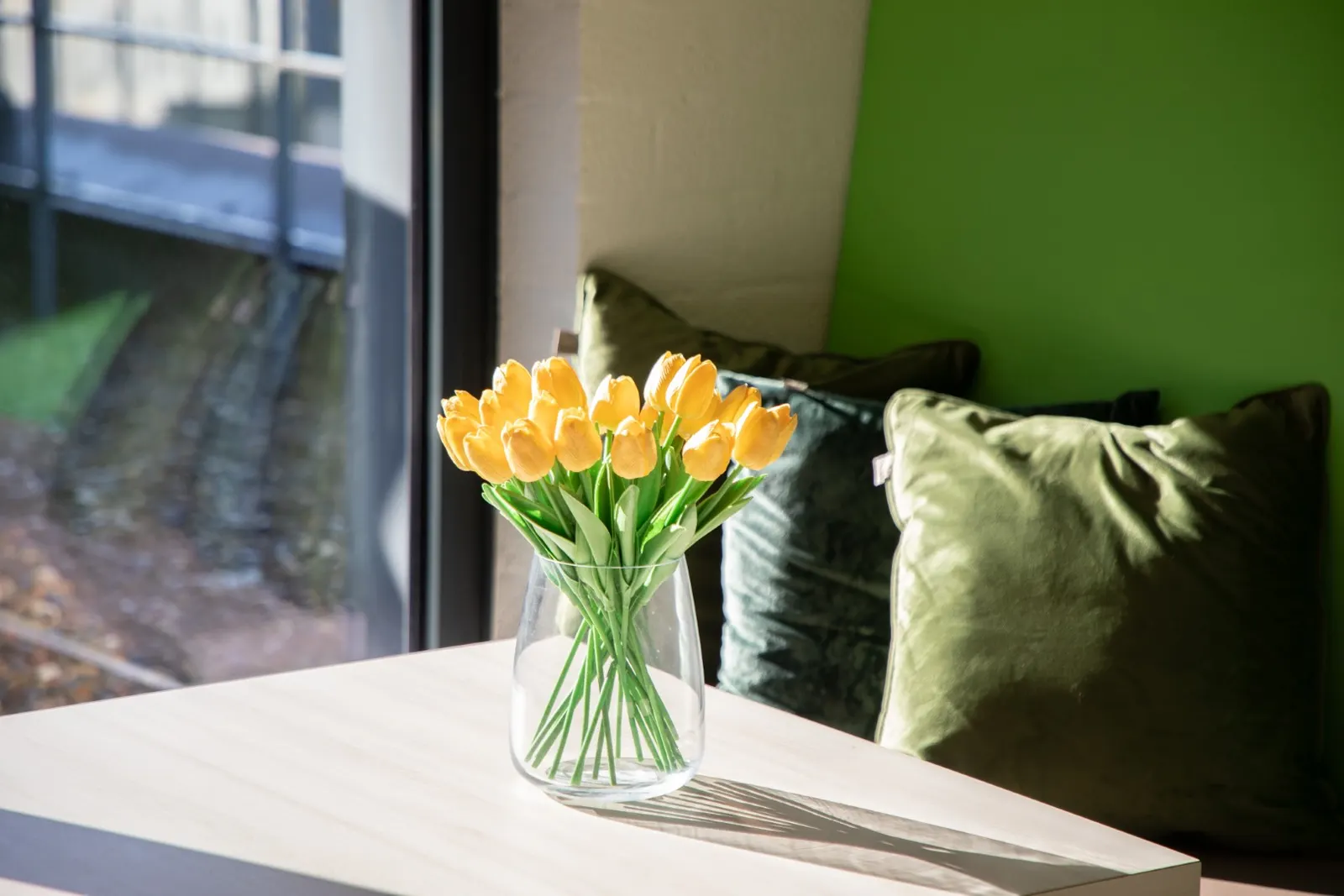 Vaas met gele tulpen op een vensterbank bij een groen kussen in Office Capital Hasselt
